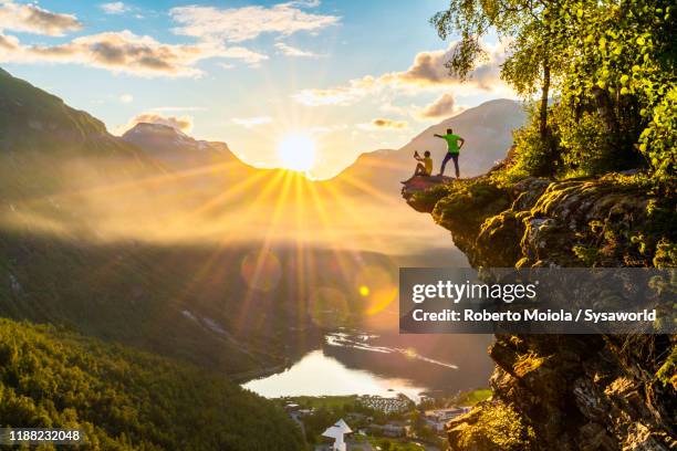 two hikers admiring geiranger fjord from top of cliff, norway - geiranger stock-fotos und bilder