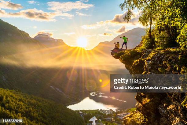 two hikers admiring geiranger fjord from top of cliff, norway - westelijke fjorden noorwegen stockfoto's en -beelden
