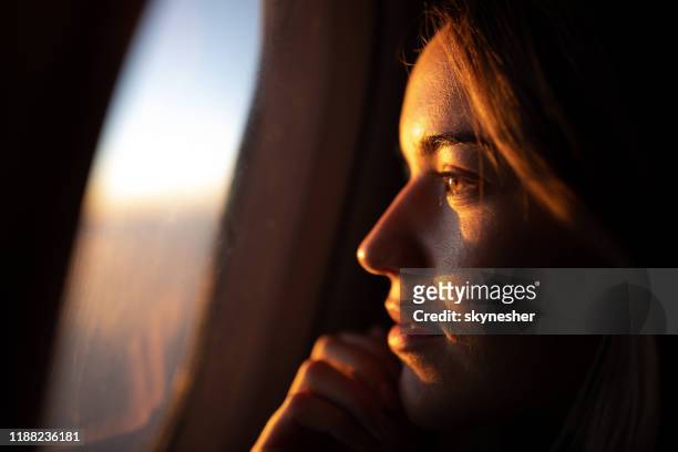 nahaufnahme von nachdenklichen frau blick auf sonnenuntergang durch flugzeugfenster. - fenster stock-fotos und bilder