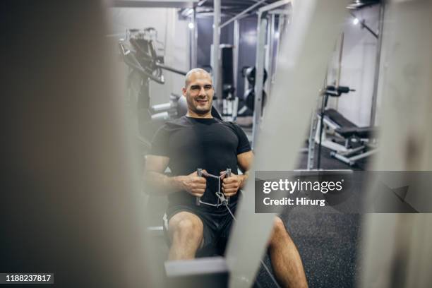 muscular man exercising on rowing machine - trx machine stock pictures, royalty-free photos & images