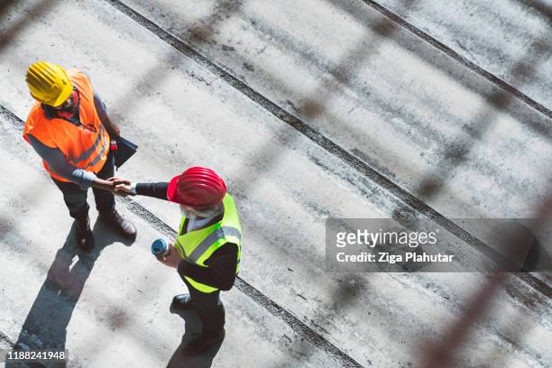 over the head view of two architects shaking hands on construction site - quality control inspectors stock pictures, royalty-free photos & images