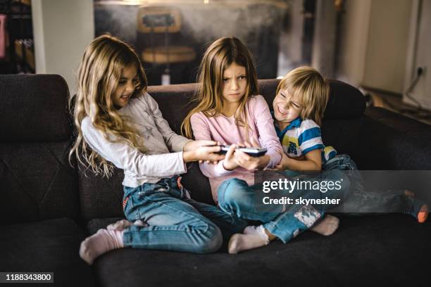 kleine geschwister kämpfen um eine fernbedienung im wohnzimmer. - sibling stock-fotos und bilder