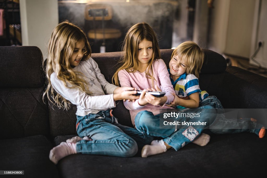 Kleine broers en zussen vechten over een afstandsbediening in de woonkamer.