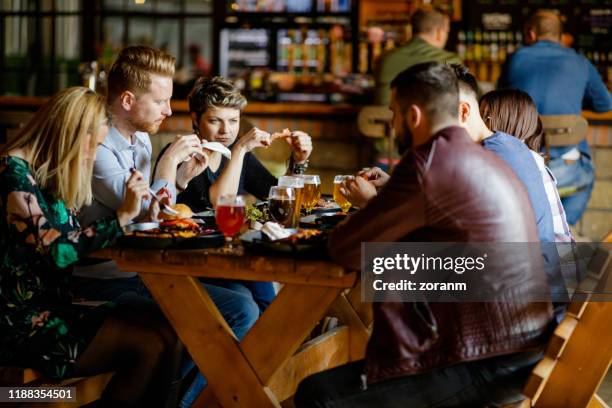 friends having dinner at the table in a pub after work - barbecue restaurant stock pictures, royalty-free photos & images