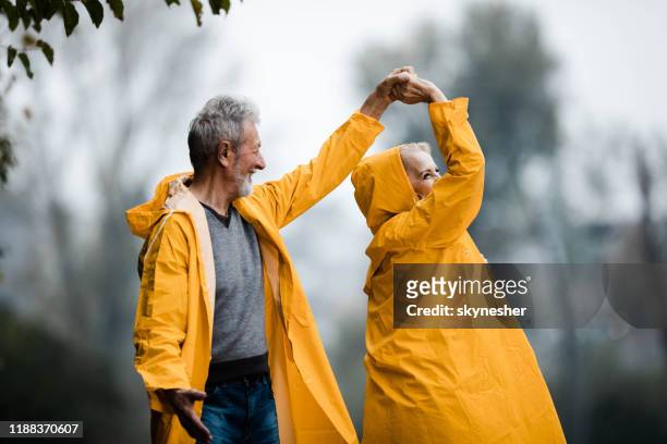 gelukkig senior paar in regenjassen dansen in het park. - mature couple winter outdoors stockfoto's en -beelden