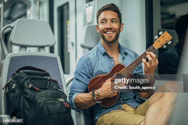 handsome mann spielt ukelele in u-bahn-zug - ukulele stock-fotos und bilder