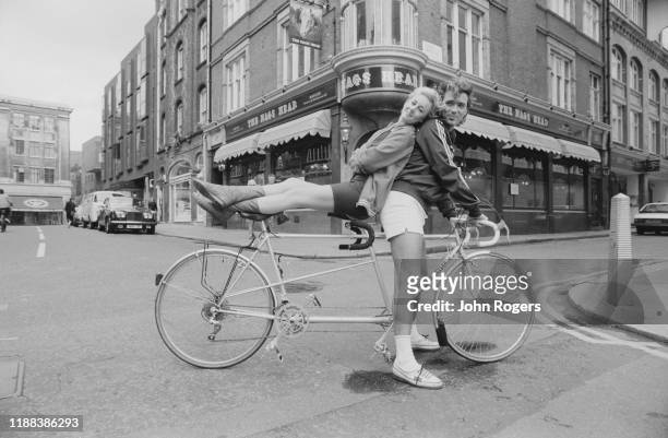 English singer Shirlie Holliman and English actor, director, and musician Martin Kemp on a tandem bike in front of the Nags Head pub in Covent...
