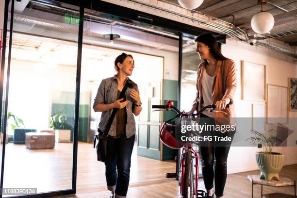 coworkers walking with bicycle on office lobby - motorcycle rider stock pictures, royalty-free photos & images