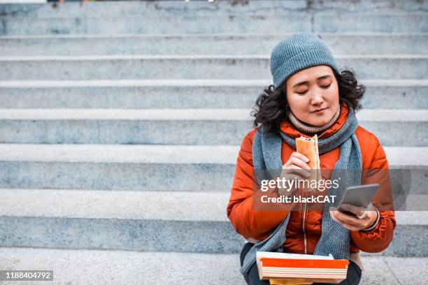 porträt einer asiatischen frau, die fast food isst - asian eating hotdog stock-fotos und bilder