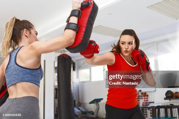 young female boxer in gym punching bag wearing boxing gloves - boxercise stock pictures, royalty-free photos & images