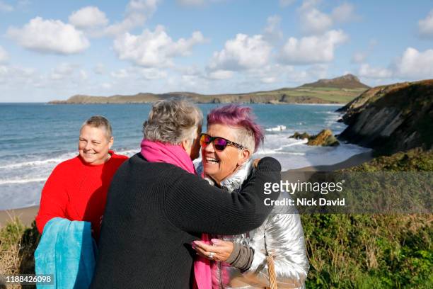 A group of women swimmers embrace and laugh on a coastal path over looking the sea