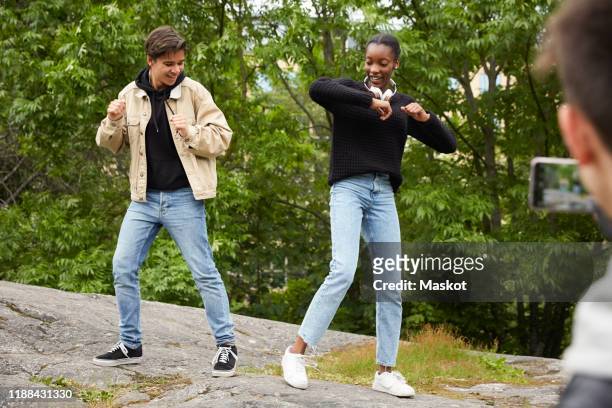 cropped image of teenage boy photographing friends dancing on rock at park - young men dance stock pictures, royalty-free photos & images