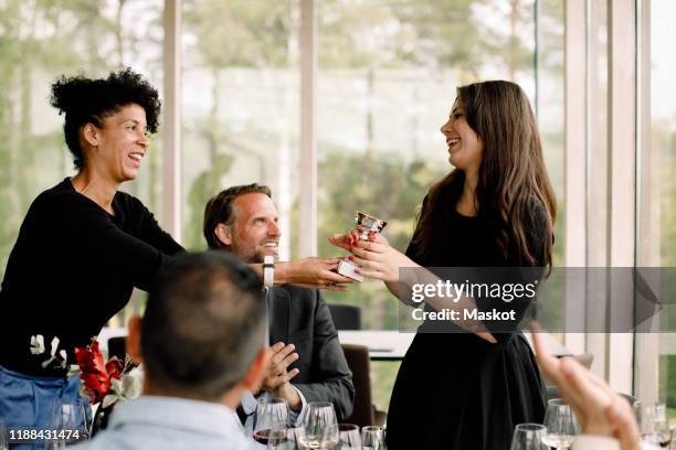 smiling businesswoman giving trophy to female colleague during kick off meeting at convention center - awards inside stockfoto's en -beelden