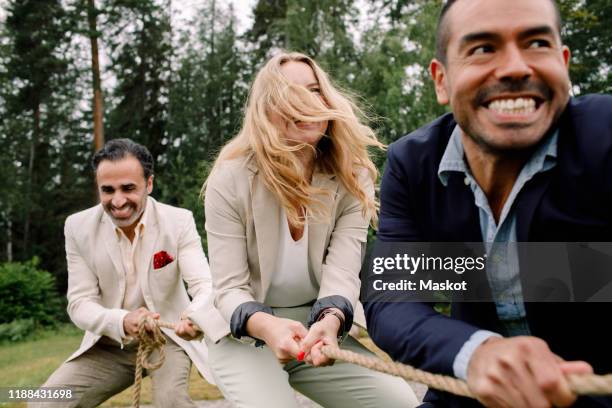 smiling male and female colleagues pulling rope while playing tug-of-war - arrastar imagens e fotografias de stock