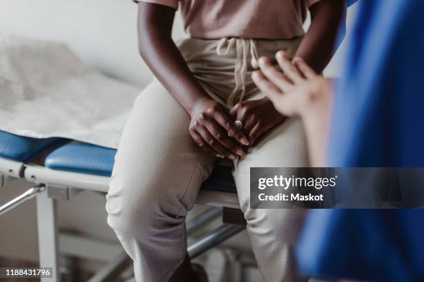 midsection of female healthcare worker explaining to young patient in medical clinic - mittlerer teil stock-fotos und bilder