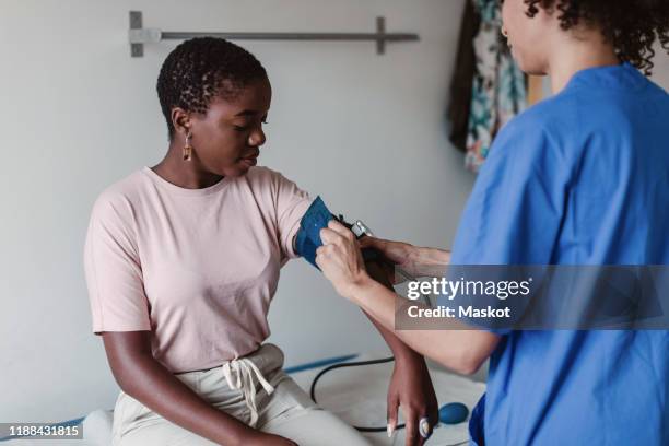 nurse checking blood pressure of female patient in clinic - hypertensive stockfoto's en -beelden