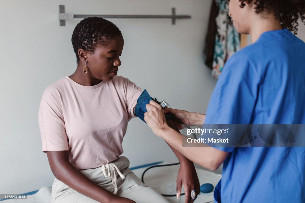 Nurse checking blood pressure of female patient in clinic