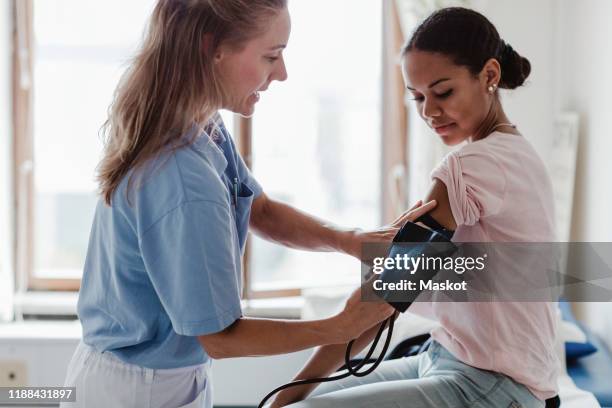 mature nurse checking patient's blood pressure in examination room at clinic - blood pressure stock-fotos und bilder