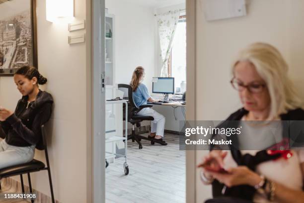 females using mobile phones while waiting outside medical examination room - patients in doctors waiting room stockfoto's en -beelden