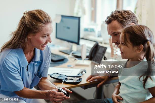 smiling girl looking at doctor showing glaucometer in medical examination room - medical examination room stockfoto's en -beelden