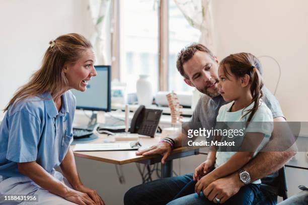 female doctor talking to girl sitting with father in medical clinic - family pediatrician stock pictures, royalty-free photos & images