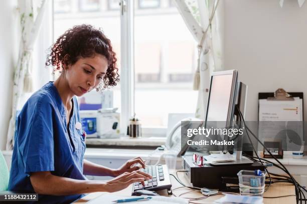 side view of female nurse making medical report in computer at clinic - medisch dossier stockfoto's en -beelden