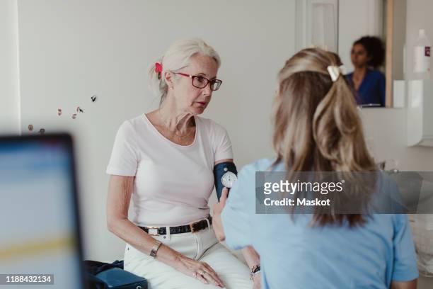 female doctor checking blood pressure of senior woman in clinic - hypertension stock-fotos und bilder