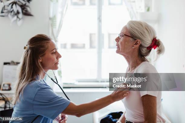 side view of female doctor examining senior patient in medical clinic - naar de hartslag luisteren stockfoto's en -beelden