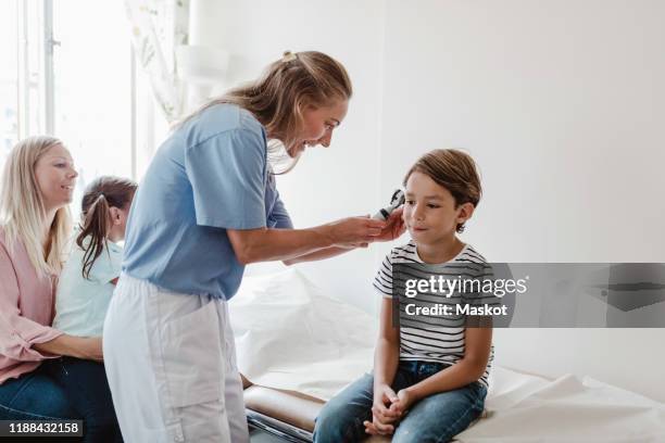 female doctor examining boy's ear with otoscope while family sitting in medical room - human ear bildbanksfoton och bilder