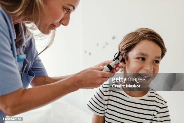 doctor examining boy's ear with otoscope in medical examination room - otoscope fotografías e imágenes de stock