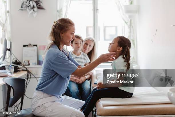 female doctor examining throat of girl while family sitting in medical room - pediatrician bildbanksfoton och bilder