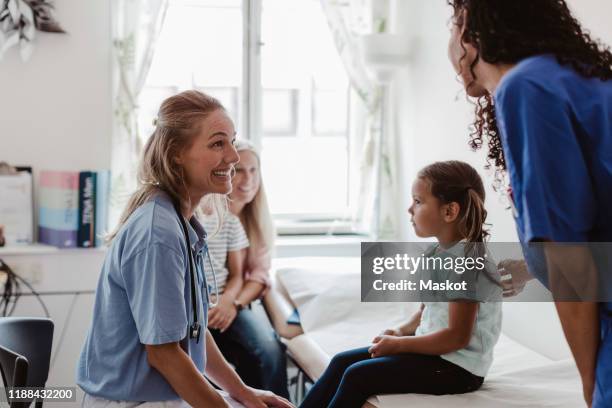 cheerful pediatrician talking to nurse while examining girl in medical clinic - infermiera foto e immagini stock