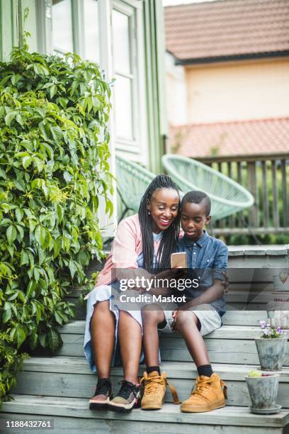 full length of happy mother and son looking at smart phone while sitting on steps - 7 steps stockfoto's en -beelden