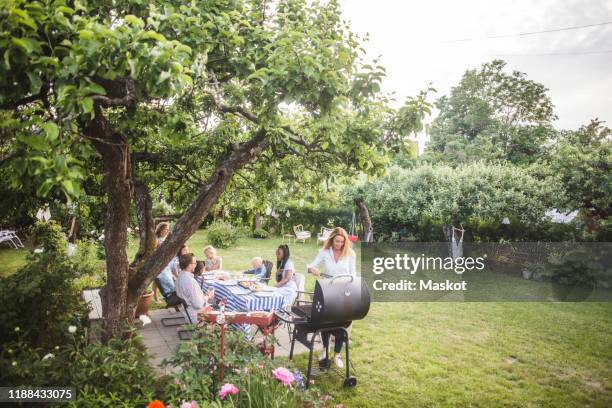 female preparing food o barbecue while family sitting by table in backyard - backyard barbeque stockfoto's en -beelden