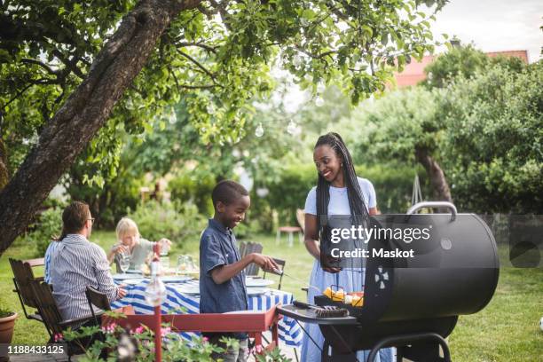 mother and son preparing food on barbecue grill in yard during weekend party - summer grilling stock pictures, royalty-free photos & images