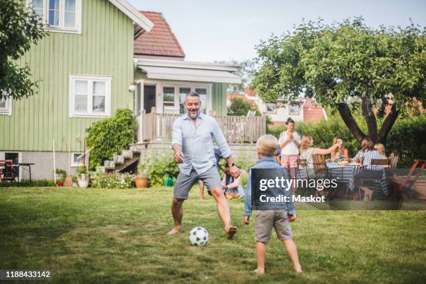 father playing football with son while friends having fun at table in backyard party - ball on a table stock-fotos und bilder