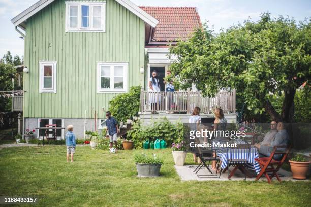 mature friends having garden party while children playing in backyard during summer weekend - backyard barbecue stock-fotos und bilder