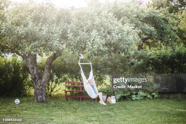 full length of boy swinging in backyard during summer weekend - swing bildbanksfoton och bilder