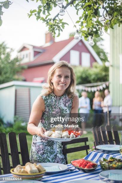 portrait of smiling mature woman holding food plate by table in backyard - white plate stock pictures, royalty-free photos & images