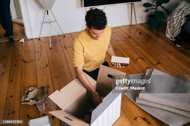 high angle view of man removing novels from cardboard box at new home - first apartment stock pictures, royalty-free photos & images