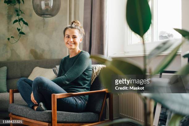 portrait of smiling woman sitting on armchair at home - 30 34 years stock pictures, royalty-free photos & images