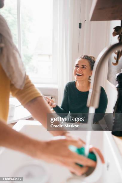 cheerful woman looking at boyfriend washing utensils at home - 水喉水 個照片及圖片檔