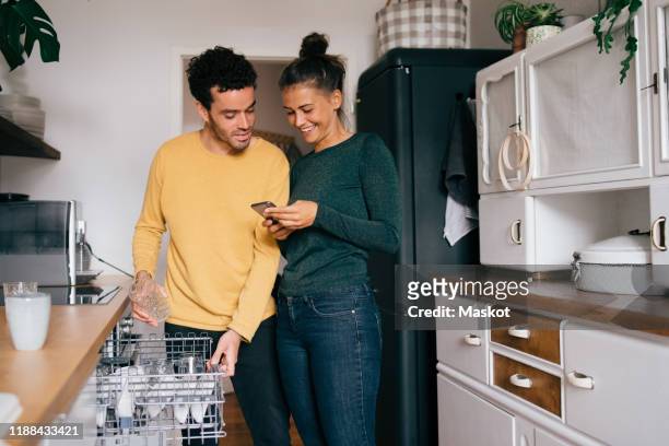 woman smiling while showing smart phone to boyfriend while standing in kitchen - smartphone zuhause stock-fotos und bilder