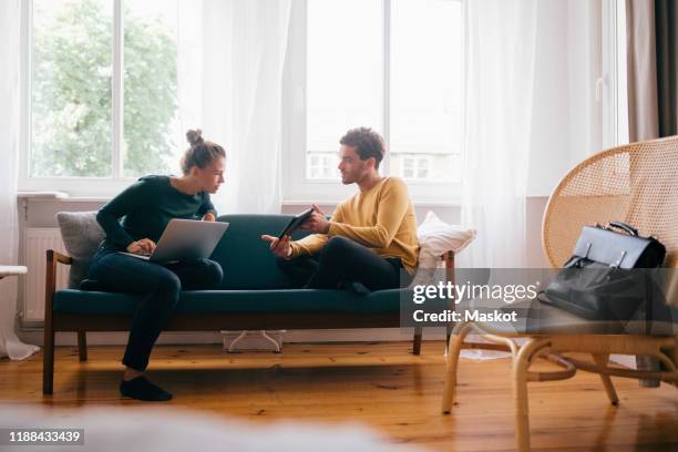 boyfriend showing digital tablet to girlfriend while sitting on sofa at home - couch laptop stock-fotos und bilder