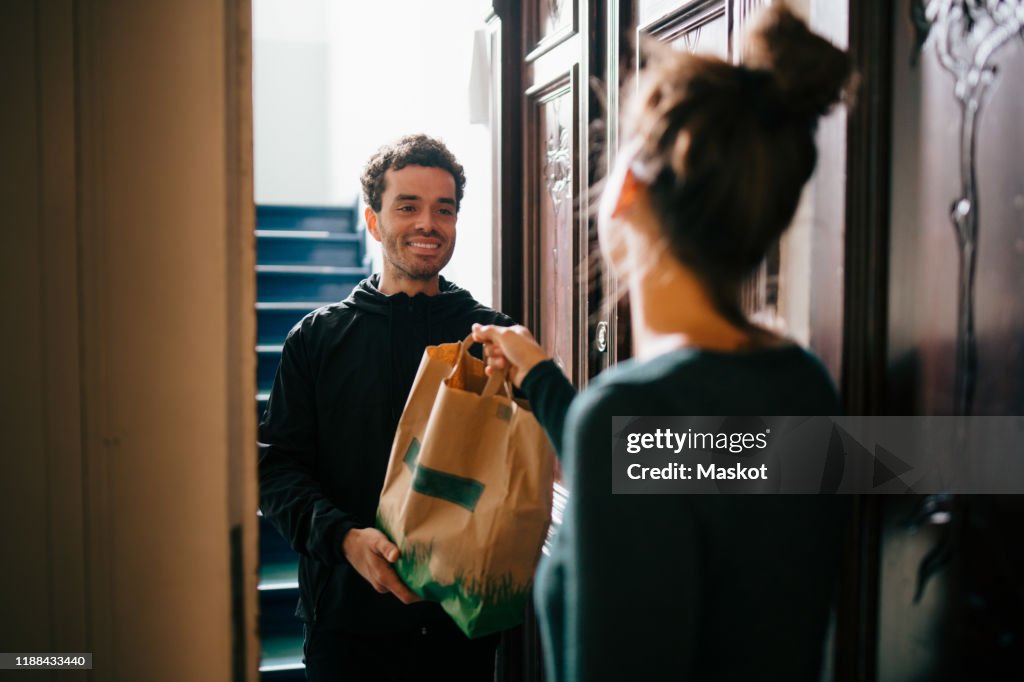 Smiling delivery man delivering bag to woman standing at doorway