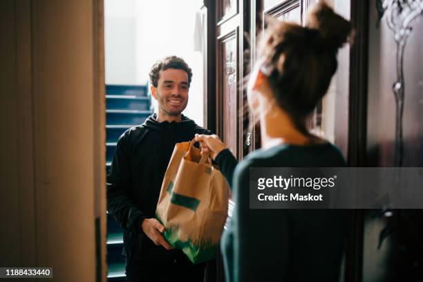 smiling delivery man delivering bag to woman standing at doorway - livre photos et images de collection