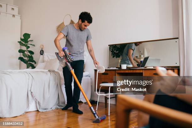 full length of man cleaning bedroom with vacuum cleaner - donna delle pulizie foto e immagini stock
