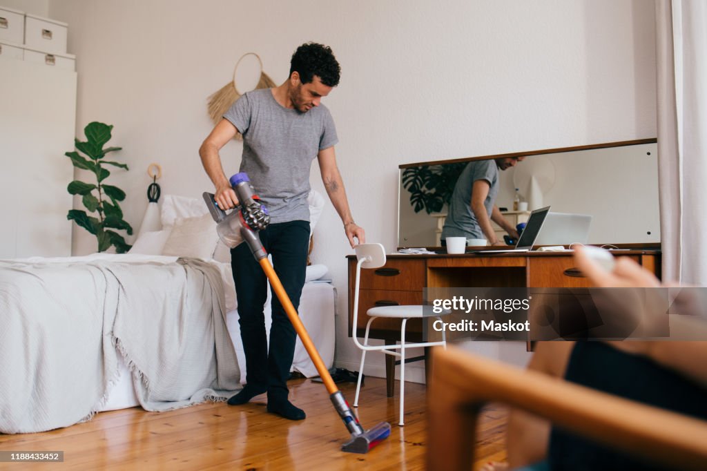 Full length of man cleaning bedroom with vacuum cleaner