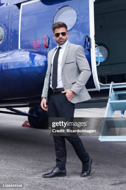 latino man in very elegant gray and blue dress standing next to a blue helicopter - billionaire stock pictures, royalty-free photos & images