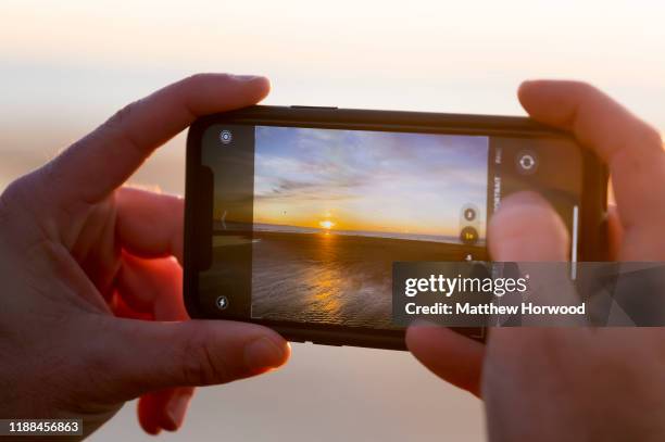 Man photographs a sunset with an Apple iPhone 11 Pro at Southerndown on November 18, 2019 in Bridgend, United Kingdom.